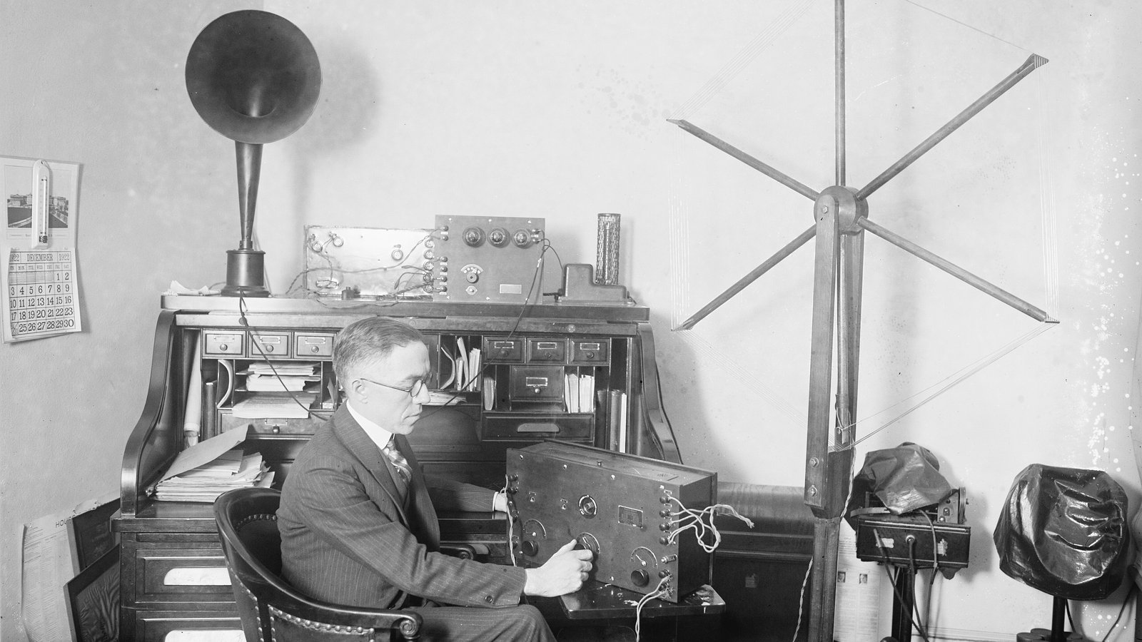 Masasındaki radyo alıcısının başında, yanında boru hoparlör ve anteniyle yayın dinleyen bir adam, 1922