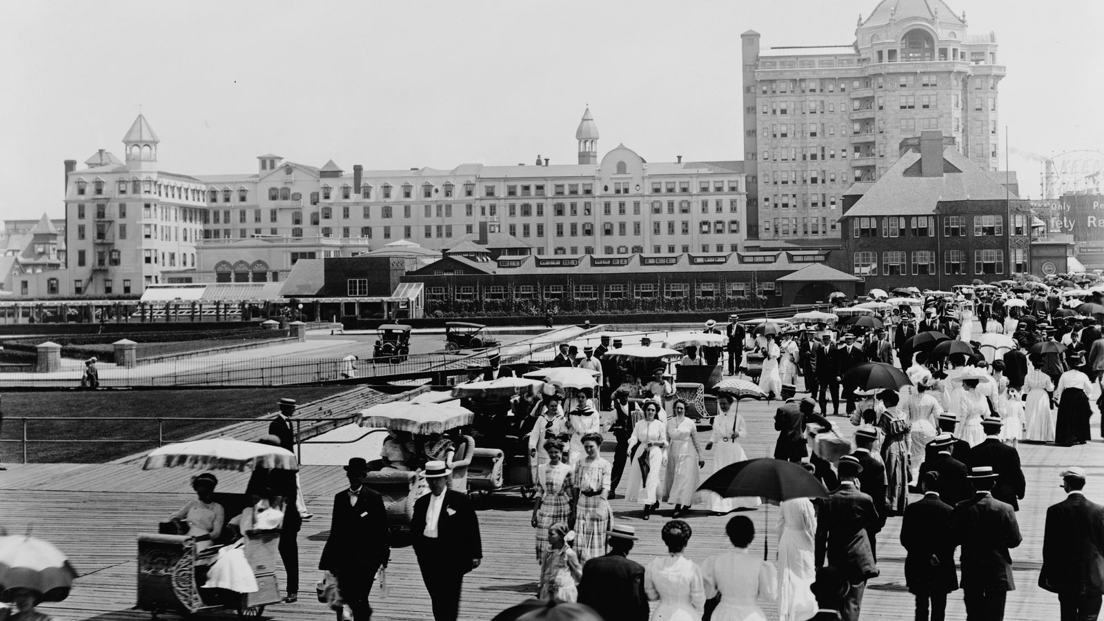 Atlantic City'de 1910 civarı bir yaz günü: güneş şemsiyeli, beyaz giysili kalabalık tahta iskelede yürüyor, arkada Traymore Oteli