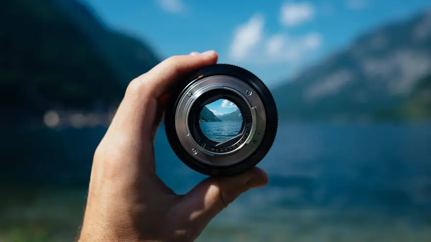 Göl ve dağ manzarasına doğru tutulan, arkasını net gösteren fotoğraf makinesi objektifi