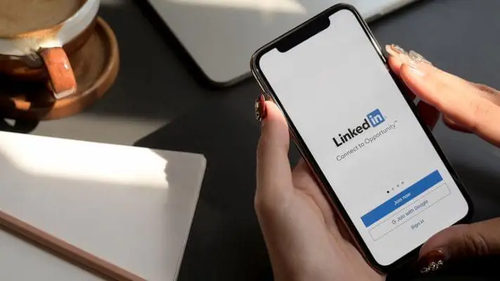 Masada iki elle tutulan akıllı telefonda açık LinkedIn uygulaması